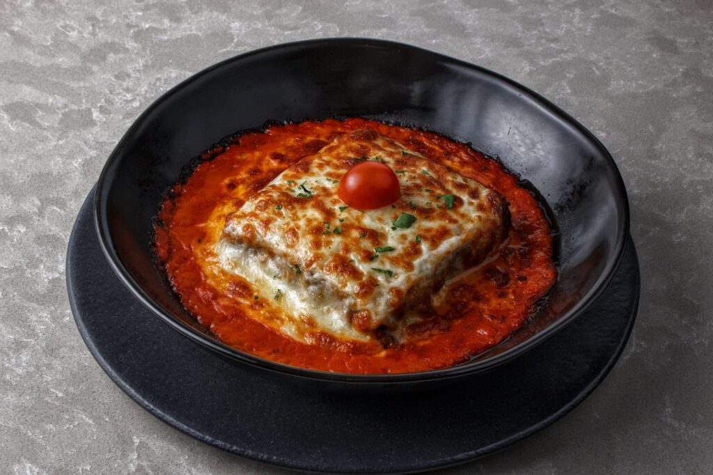 Savoureuse lasagne cuite au four avec des tomates cerises et du fromage, servie dans un bol noir avec une riche sauce tomate.