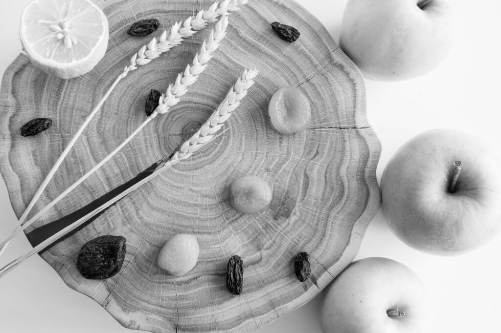 Élégante nature morte en noir et blanc mettant en scène des pommes, un citron, du blé et des raisins sur du bois.