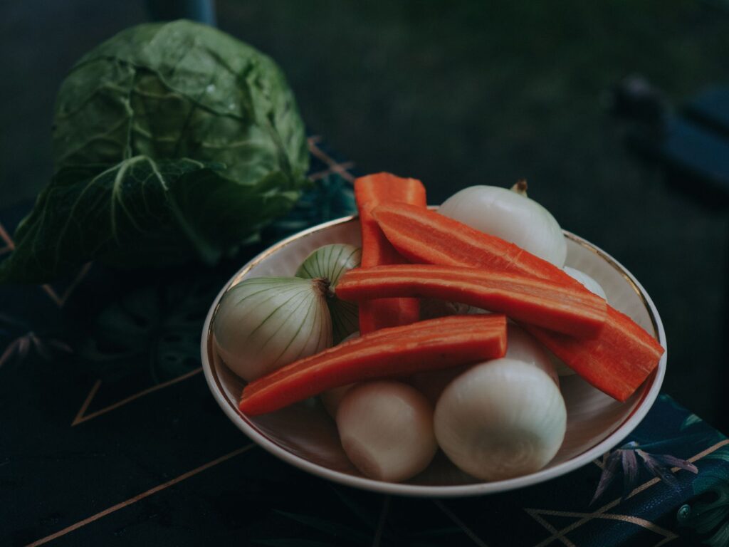 Bol de carottes et oignons frais avec du chou sur une nappe sombre et à motifs en extérieur.