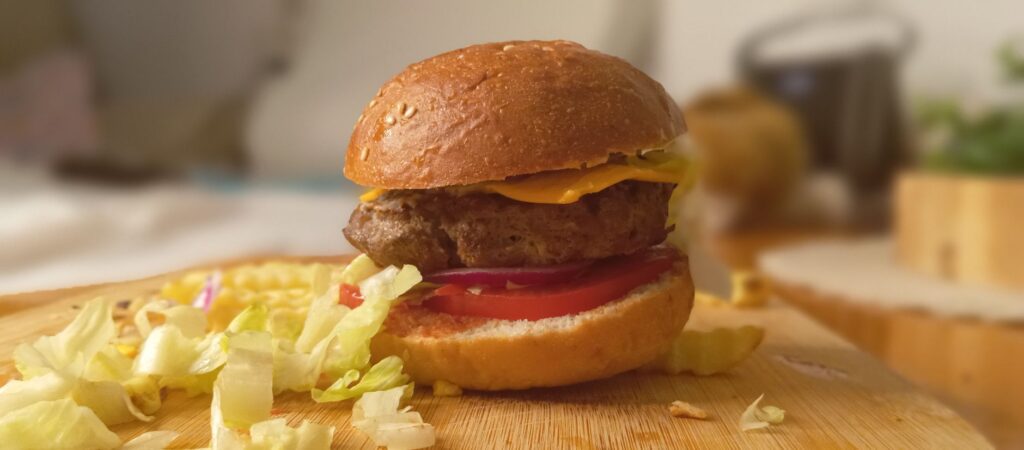 Gros plan d'un cheeseburger avec des garnitures fraîches sur une planche de bois, mettant en valeur l'attrait culinaire.