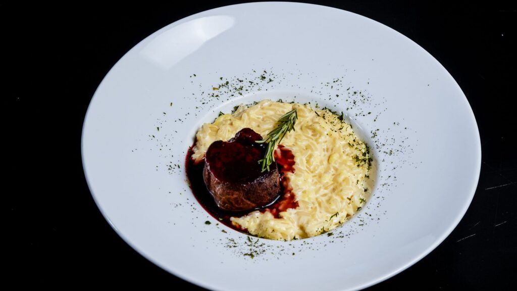 Délicieux filet de bœuf avec réduction de vin rouge et risotto crémeux sur une assiette blanche.