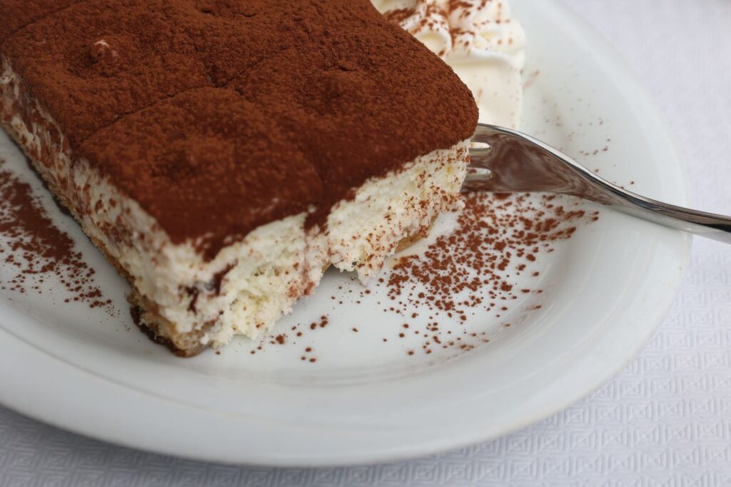 Une tranche appétissante de tiramisu recouverte de poudre de cacao sur une assiette blanche.