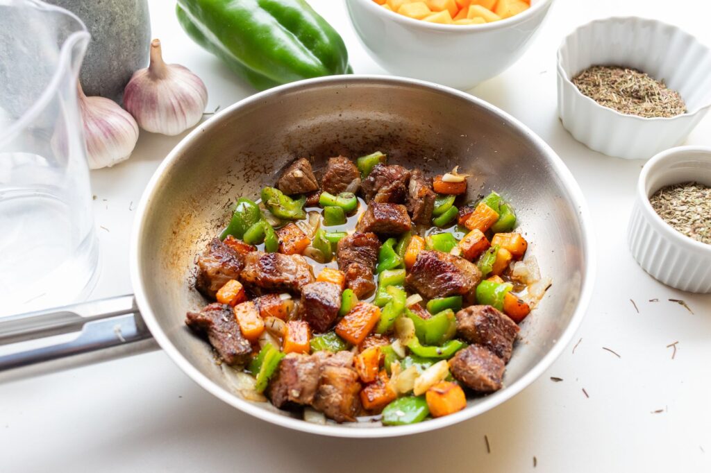 Délicieux sauté de bœuf avec poivrons et carottes dans une poêle en acier inoxydable, assaisonné d'herbes.