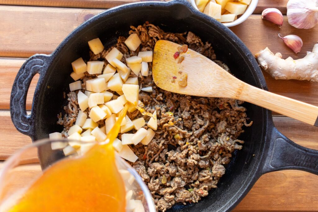 Du bœuf haché et des pommes de terre cuits dans une poêle avec du bouillon versé pour un repas copieux.
