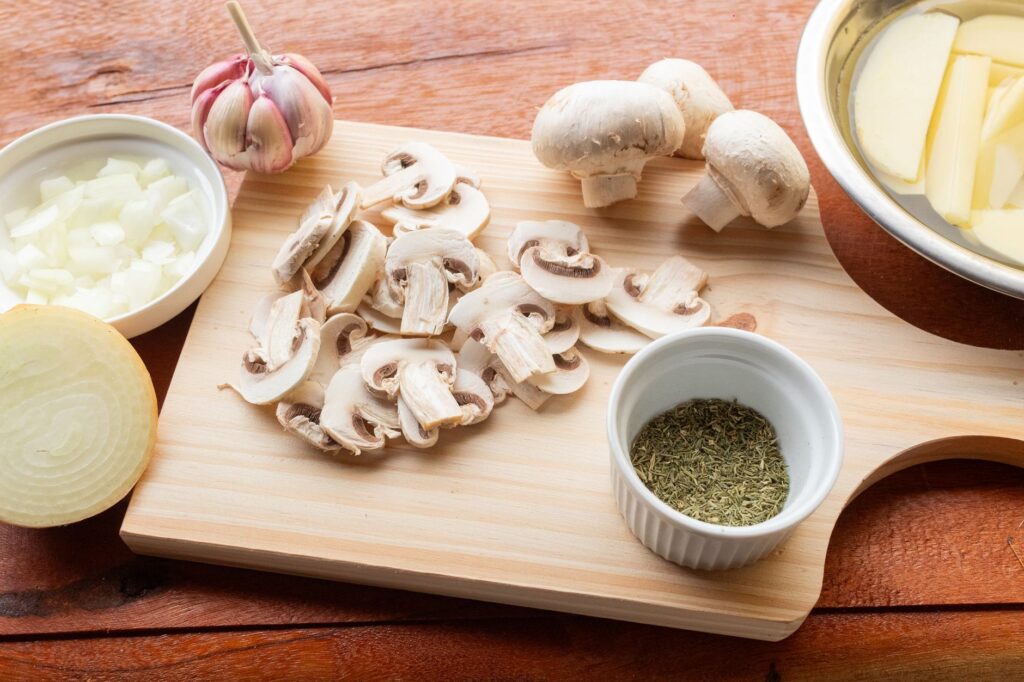 Une planche à découper en bois avec des champignons frais, de l'ail, des oignons et des herbes, prêts à être cuisinés.