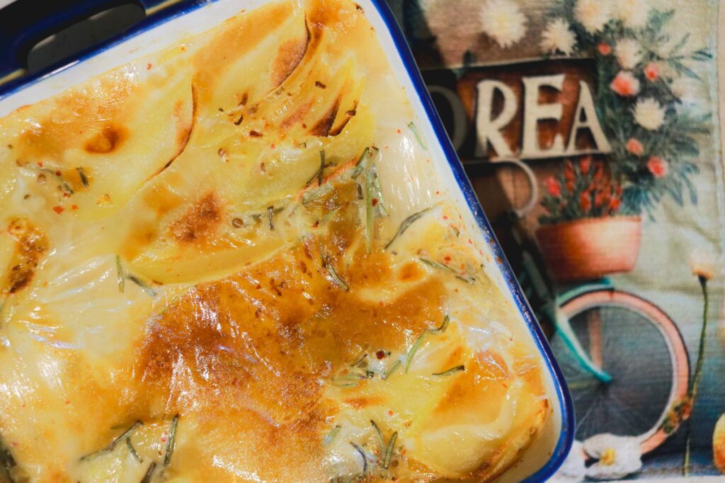 Un gratin de pommes de terre riche et crémeux, fraîchement cuit, doré et croustillant, servi dans un plat en céramique.