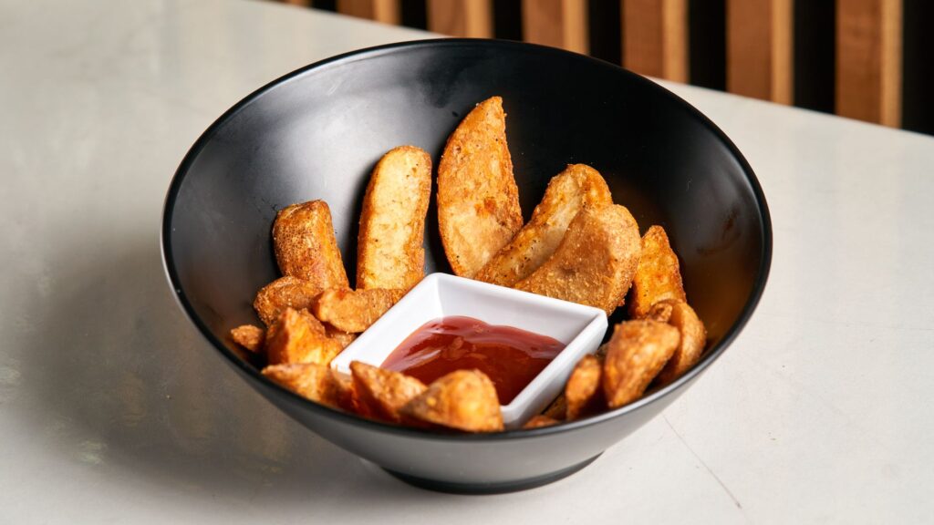 De délicieuses pommes de terre croustillantes servies avec du ketchup dans un bol noir moderne.