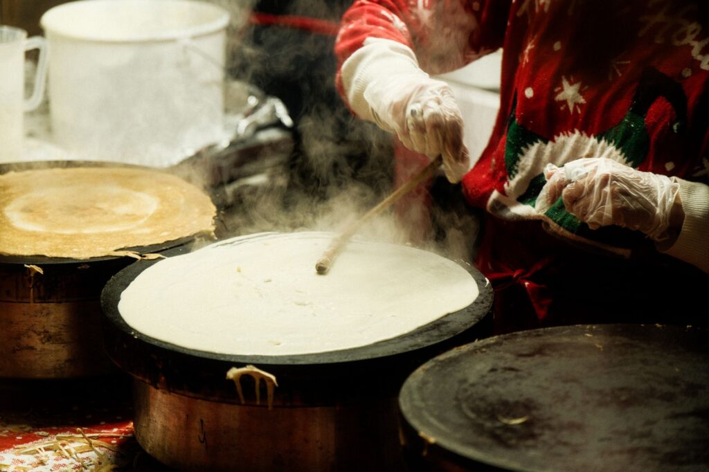 Une personne préparant des crêpes sur un stand de marché de Noël, vêtue d'un pull festif.