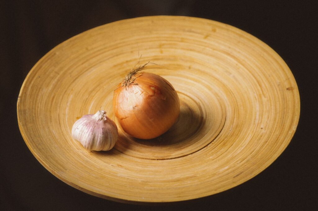 Une nature morte rustique représentant un oignon et de l'ail sur une assiette en bois, mettant en valeur des tons terreux.