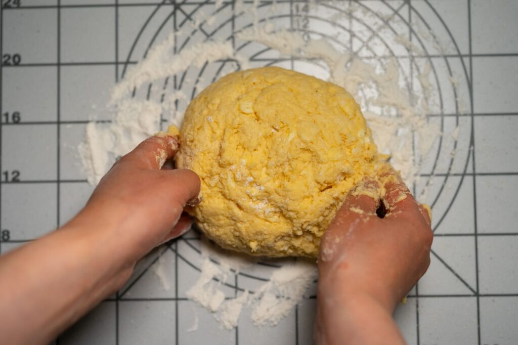 Gros plan sur des mains pétrissant une pâte à pâtes maison sur un plan de travail fariné.
