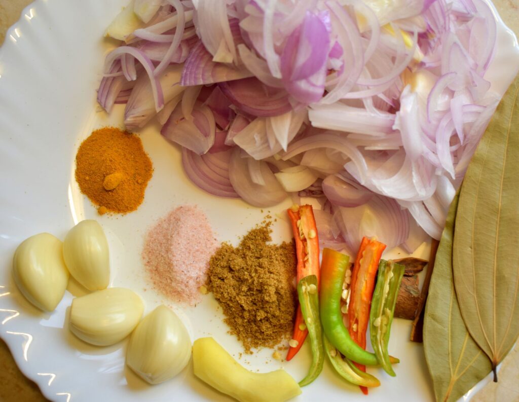 Un assortiment coloré d'oignons, d'ail, de curcuma et autres ingrédients sur une assiette, parfait pour une cuisine maison savoureuse.