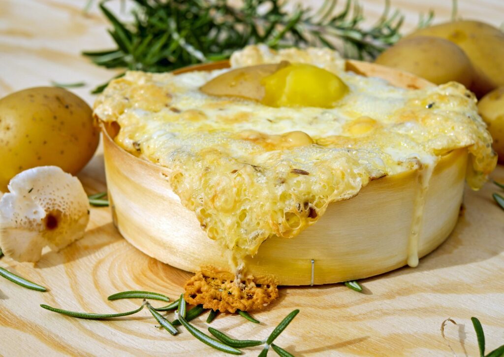 Un plat de fromage cuit au four, agrémenté de romarin, de pommes de terre et de champignons, servi sur une planche en bois et qui met l'eau à la bouche.