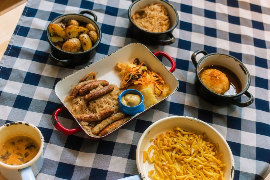 Repas traditionnel bavarois composé de saucisses, de pommes de terre, de chou et de moutarde, servi sur une nappe à carreaux.
