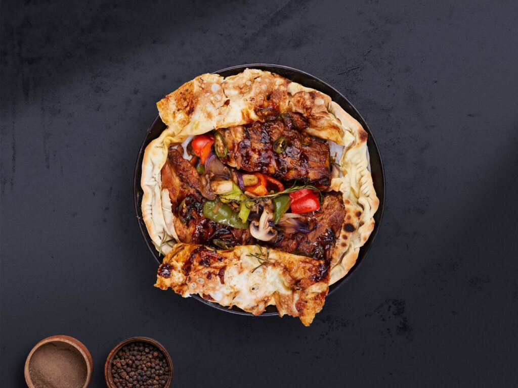 Gros plan sur une focaccia gastronomique au bœuf et aux légumes sur fond sombre.