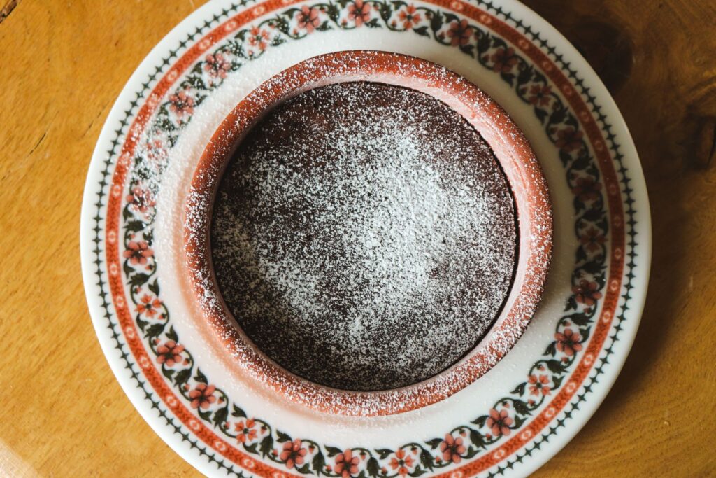 Un délicieux gâteau au chocolat saupoudré de sucre glace, servi dans un plat décoratif en céramique.
