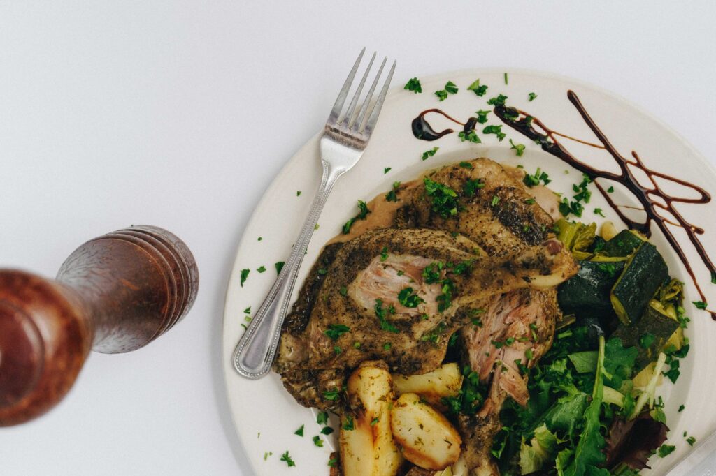 Gros plan d'un repas gourmet avec du canard rôti, des pommes de terre, des courgettes et des légumes, garni d'herbes fraîches.