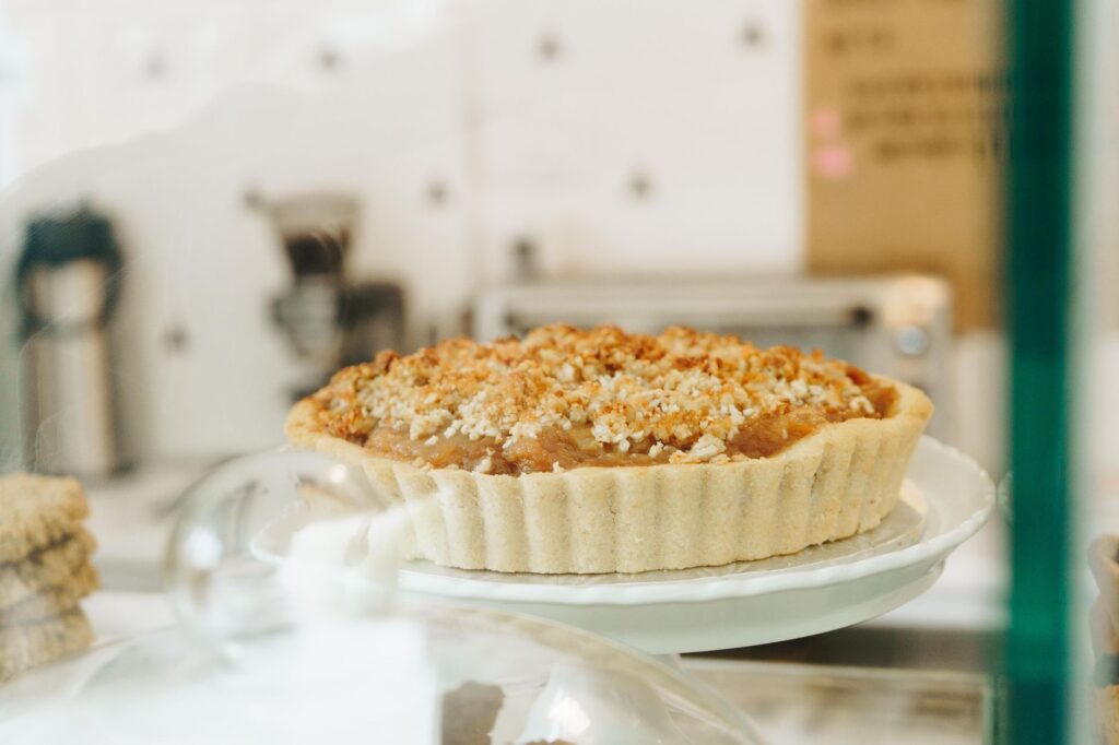 Gros plan sur une tarte aux pommes crumble fraîchement cuite en vitrine dans un café cosy.