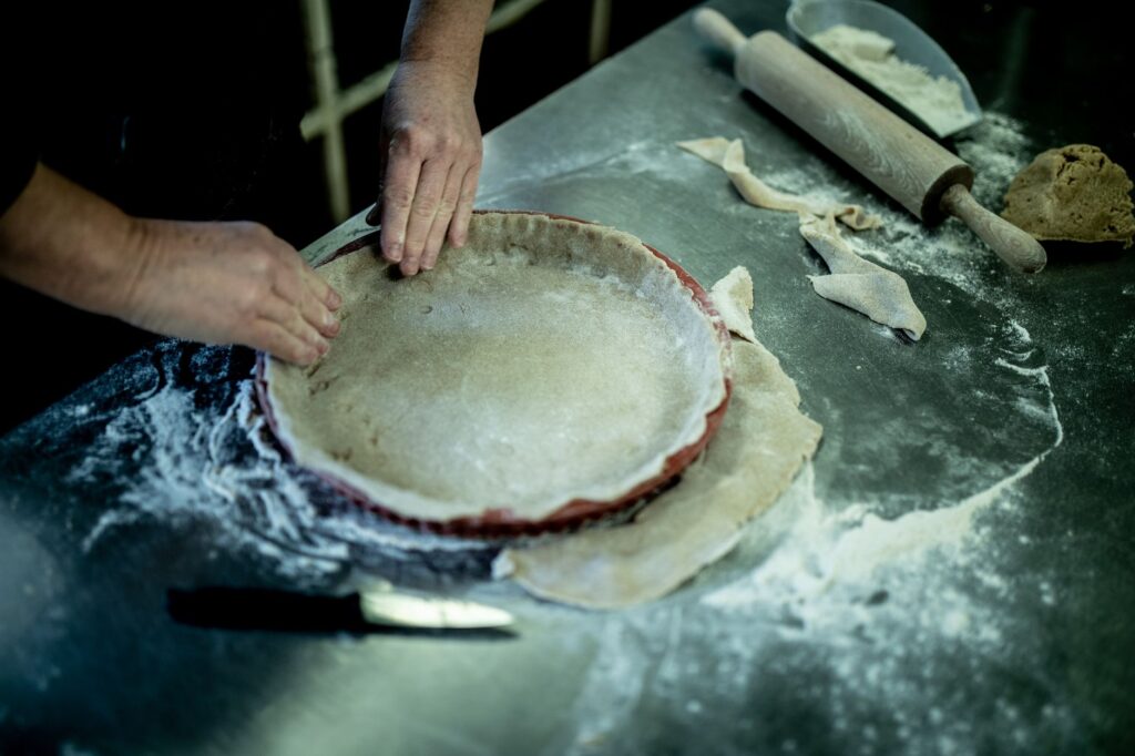 Mains d'un boulanger façonnant la croûte de tarte sur une surface farinée avec des outils dans un cadre de cuisine.