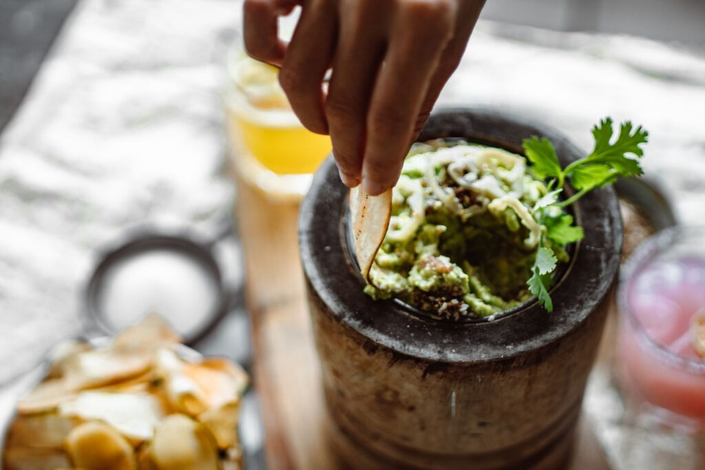 La main d'une femme trempant une puce dans une guacamole fraîche dans un bol rustique, mettant en valeur la délicieuse cuisine mexicaine.