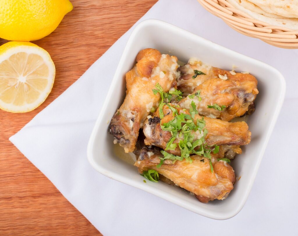 Ailes de poulet croustillantes au citron et aux herbes, garnies d'herbes fraîches dans un bol blanc.