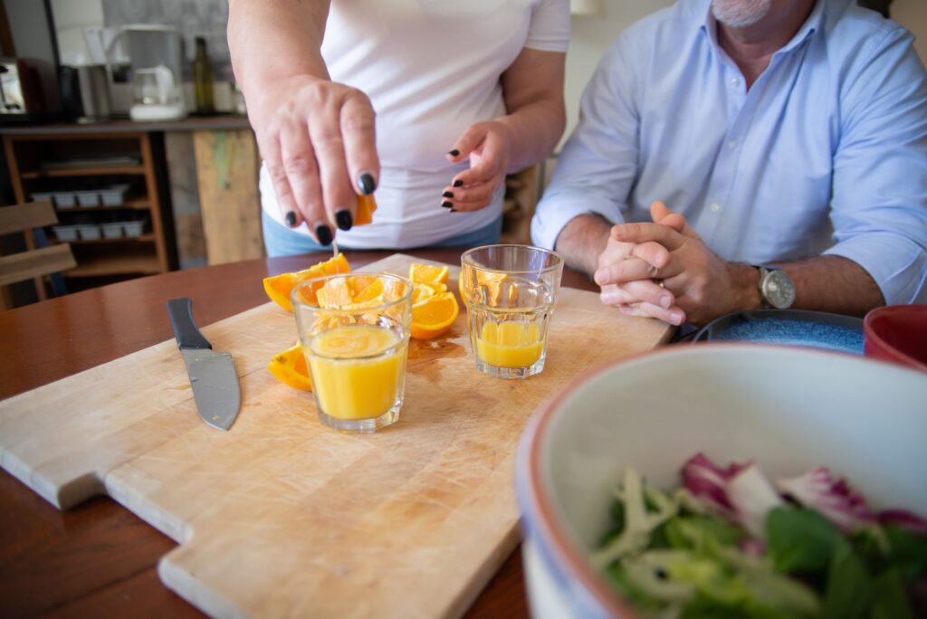Mains pressant du jus d'orange frais sur une planche à découper à l'intérieur avec des verres.