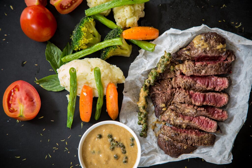 Steak grillé accompagné de légumes frais et de sauce au poivre, présentant un repas coloré et appétissant.