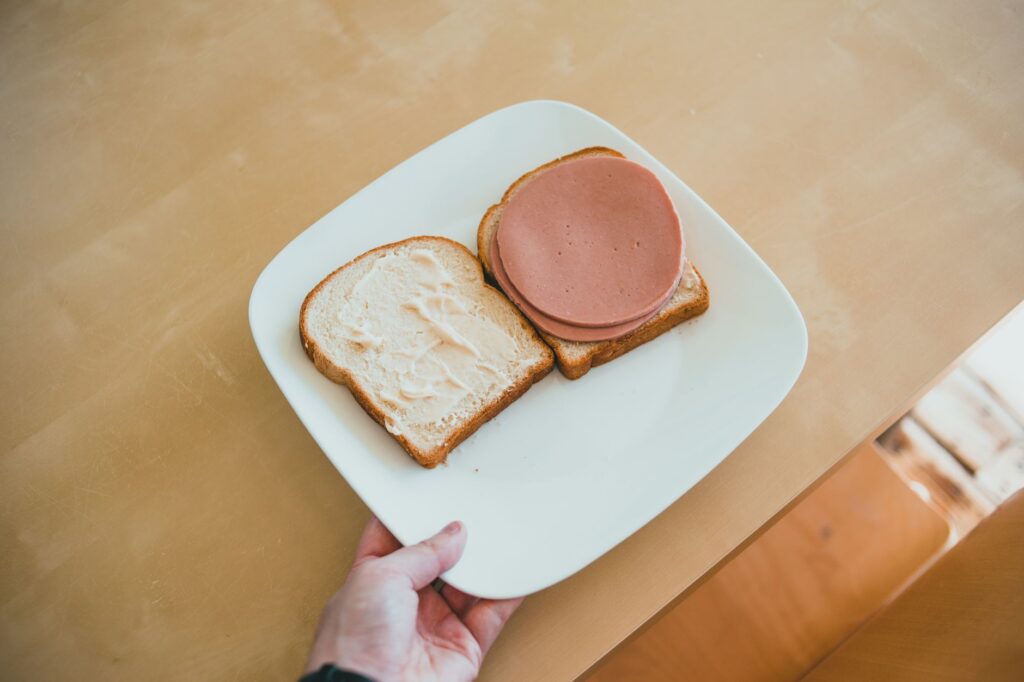 Un simple sandwich au jambon servi ouvert sur du pain avec de la mayonnaise sur une assiette blanche.