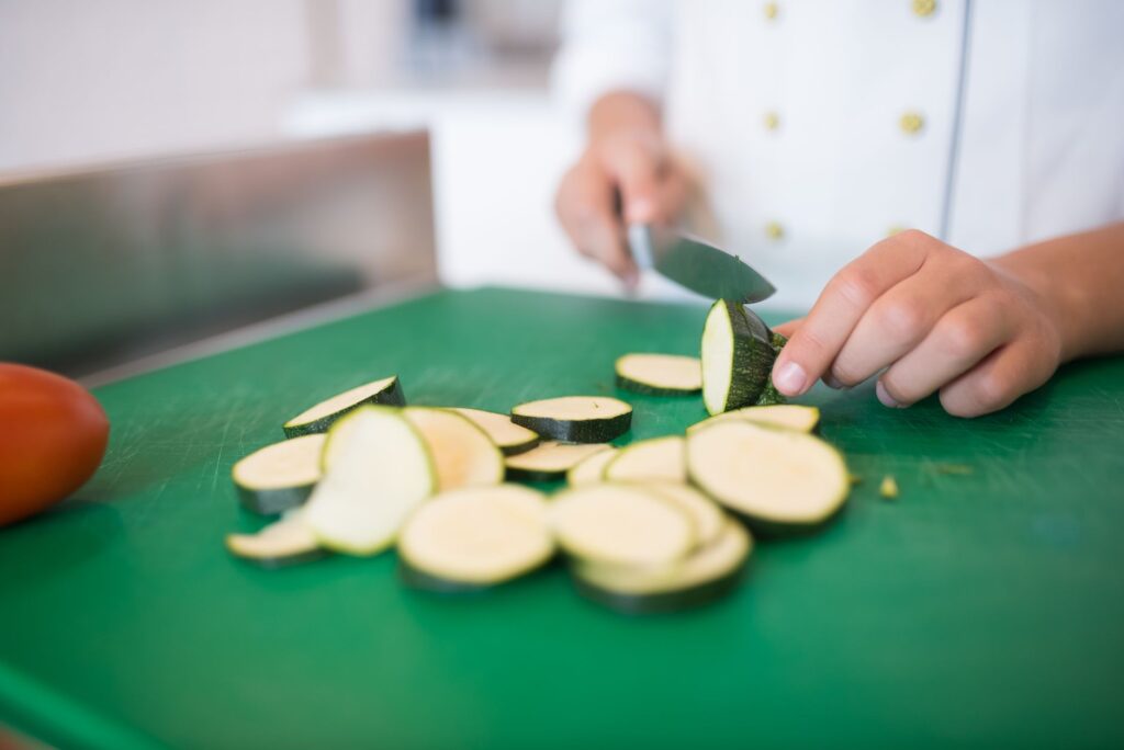 Gros plan d'un chef tranchant des courgettes sur une planche à découper verte pour une cuisine fraîche.