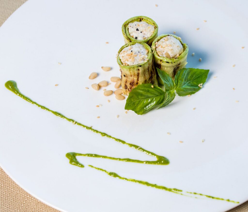 Gros plan de rouleaux de courgette gourmets avec pignons de pin et basilic sur une assiette.
