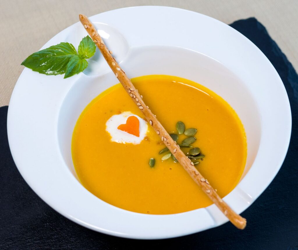 Soupe de potiron élégante garnie de crème et d'un gratte-cul au sésame, parfaite pour des visuels de restauration haut de gamme.