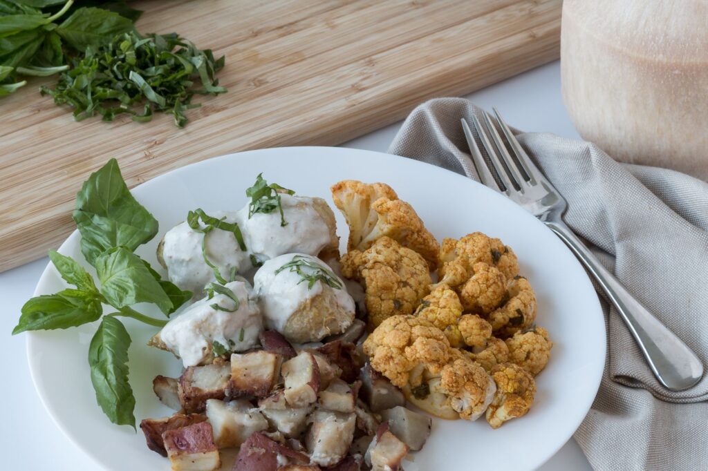 Un délicieux plat gourmet avec du chou-fleur rôti et des plats garnis de basilic sur une assiette blanche.