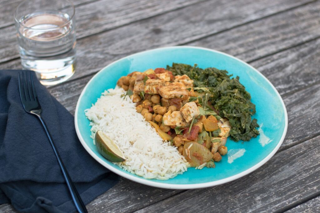 Assiette végétarienne délicieuse avec du riz, des pois chiches et des légumes verts sur une table rustique.
