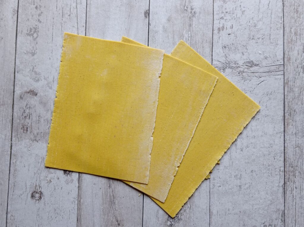 Feuilles de lasagne jaunes fraîches déposées sur une surface en bois rustique.