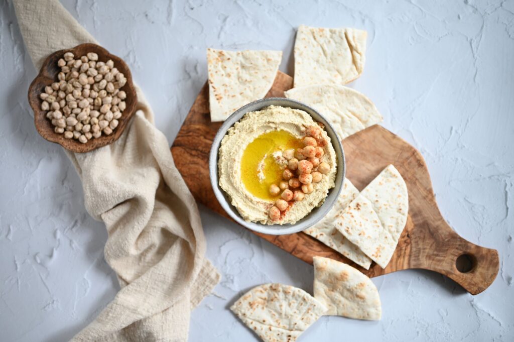 Une vue en plongée de hummus crémeux avec de l'huile d'olive, des pois chiches et du pita sur une planche en bois.