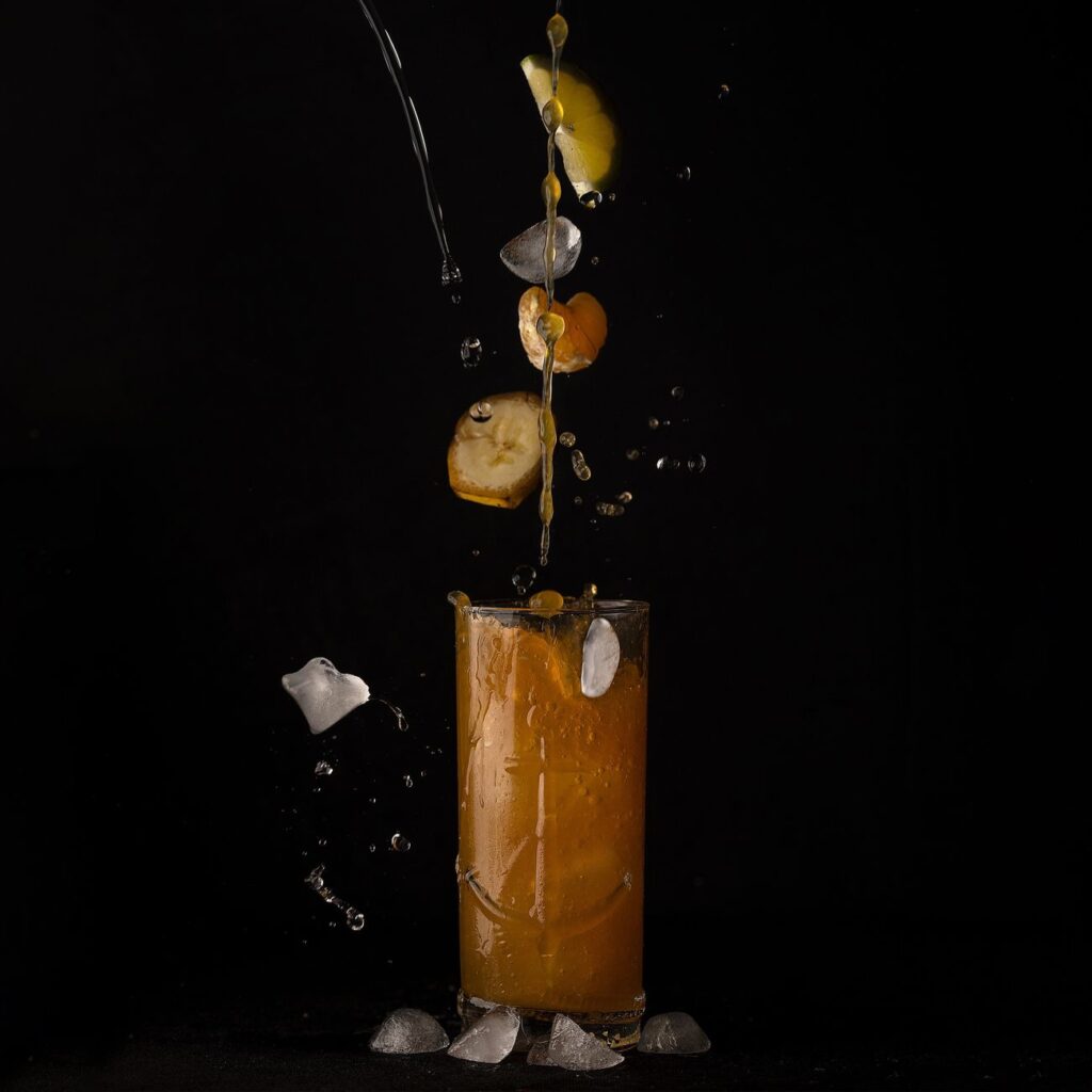 Le jus d'agrumes éclabousse avec des glaçons et des tranches de fruits sur un fond noir.