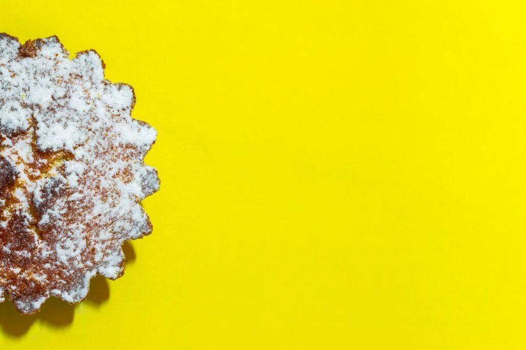 Un délicieux gâteau cuit saupoudré de sucre en poudre sur un fond jaune vif, offrant amplement d'espace pour le texte.