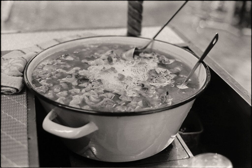 Une photo en noir et blanc au style vintage d'une casserole de soupe fumante, illustrant la cuisine rustique.