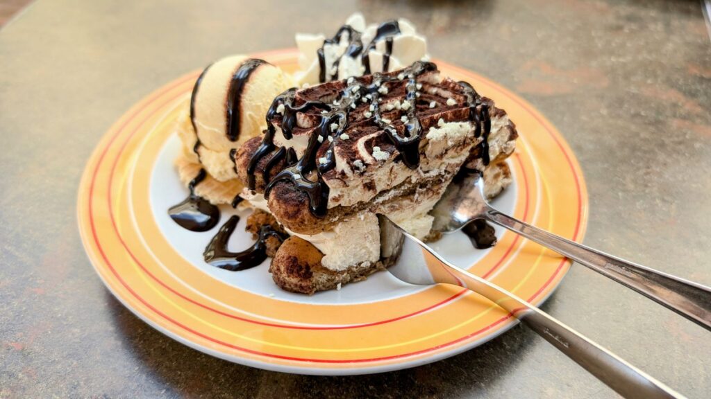 Tiramisu avec coulis au chocolat servi avec une glace vanille sur une assiette colorée, un dessert parfait.