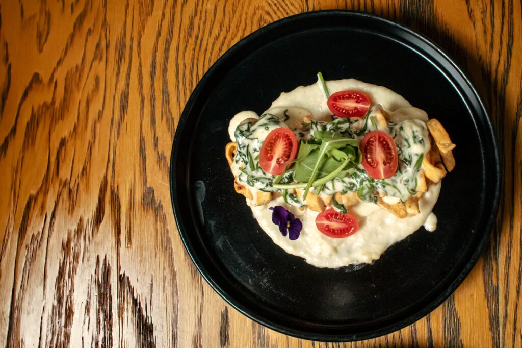Présentation élégante d'un plat gourmet avec sauce crémeuse, tomates et roquette.