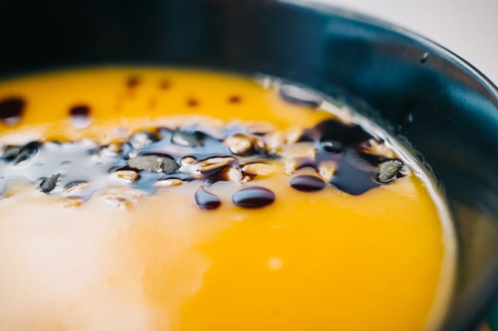 Gros plan appétissant d'une soupe crémeuse à la citrouille garnie dans un bol noir.
