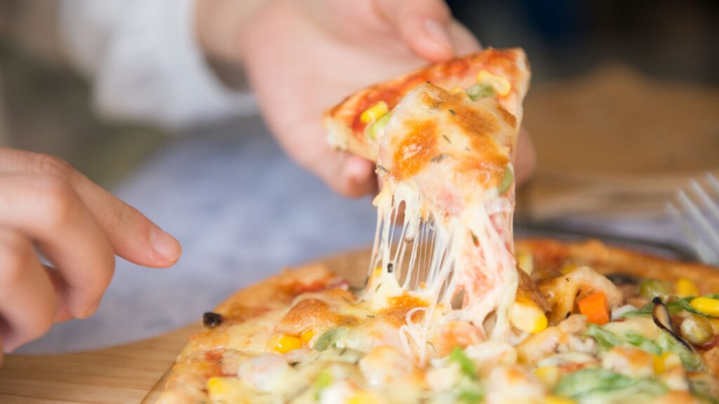 Gros plan appétissant d'une part de pizza au fromage avec des garnitures, étant tirée d'une tarte fraîchement cuite.