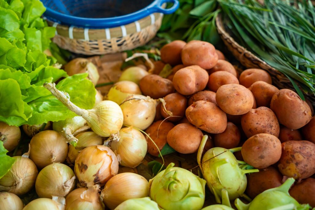 Gros plan sur un assortiment de légumes frais, y compris des oignons, des pommes de terre et des légumes verts, dans un stand de marché fermier.