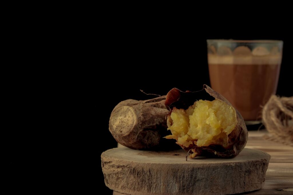 Nature morte de patate douce rôtie avec un verre de café sur une table en bois contre un fond sombre.