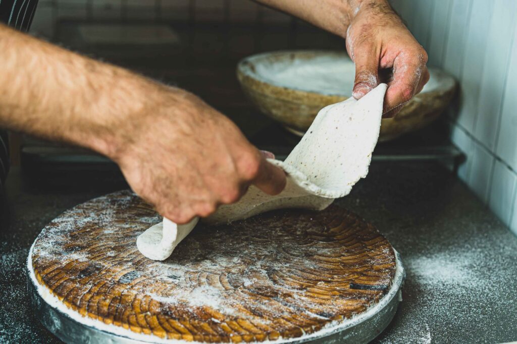 Mains d'un chef façonnant de la pâte à pizza sur une planche en bois dans un environnement de cuisine.