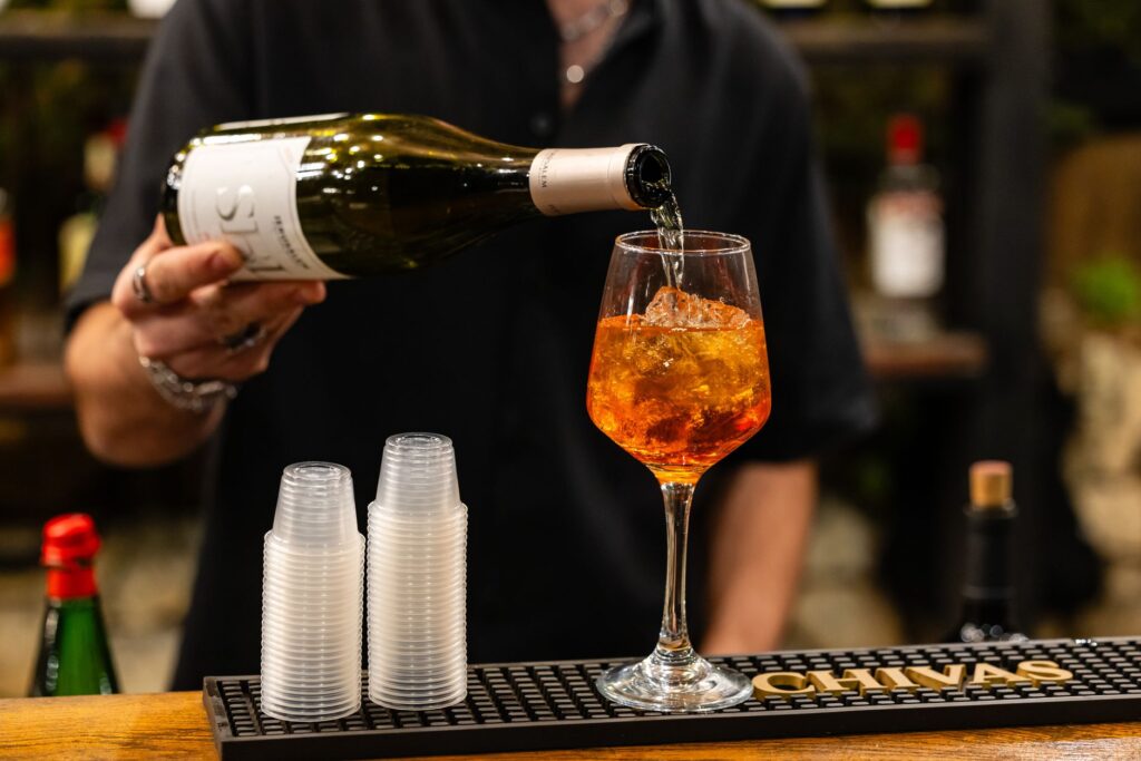 Barman versant un Aperol Spritz dans un verre, avec une couleur orange vibrante et des cubes de glace.