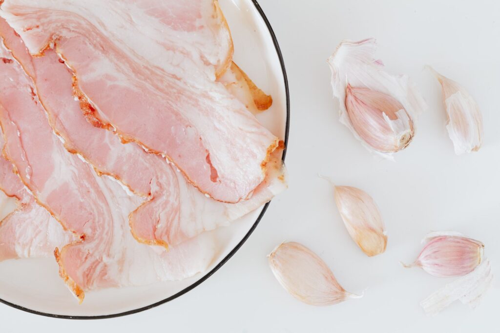 Vue de dessus de tranches de bacon frais et de gousses d'ail sur un fond blanc pour une inspiration culinaire.