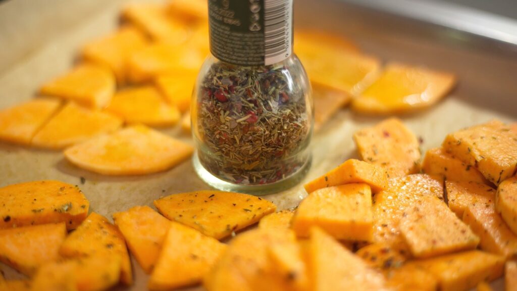 Vue en gros plan de tranches de patates douces fraîchement assaisonnées avec un flacon d'épices, parfait pour les passionnés de gastronomie.