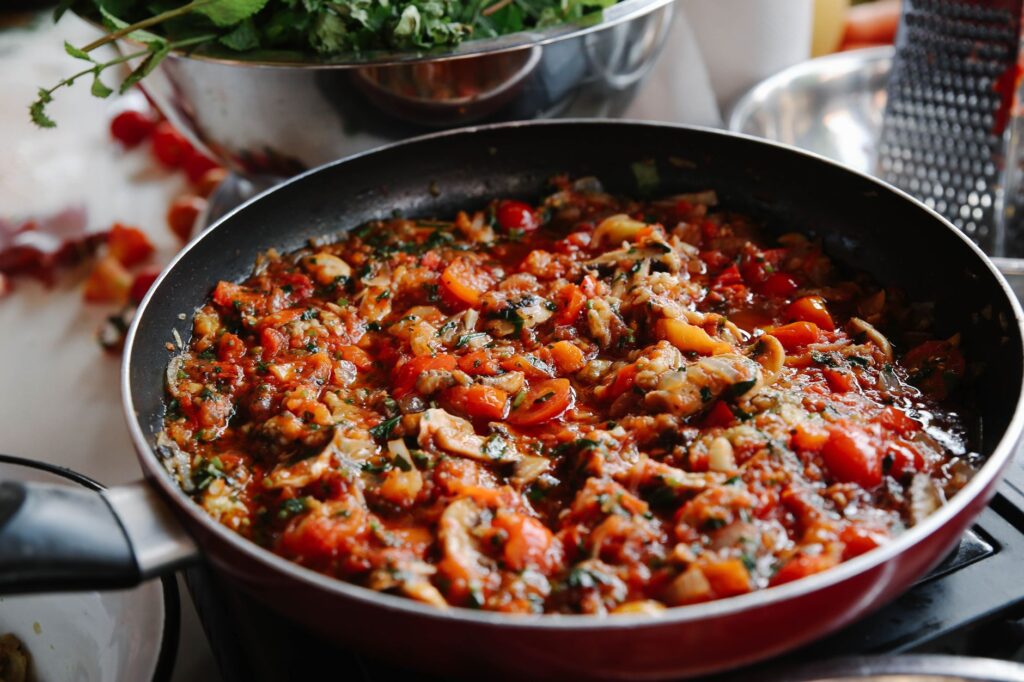Gros plan d'un plat de ratatouille vif en train de cuire dans une poêle, avec des tomates et des herbes.