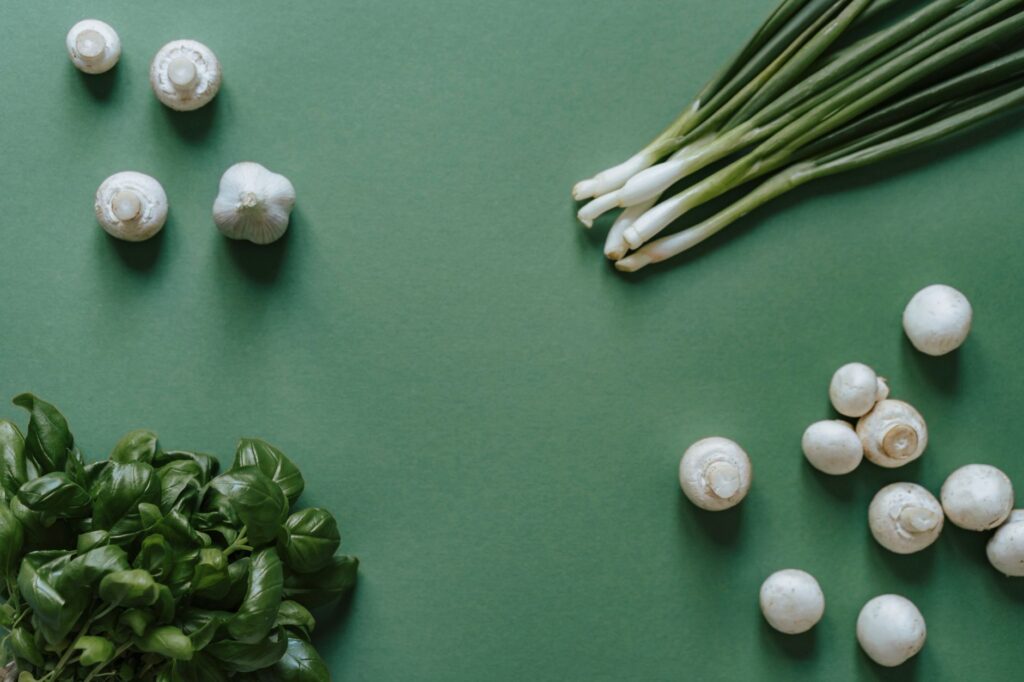 Vue de dessus d'ingrédients frais, y compris du basilic, des champignons, de l'ail et des oignons verts sur un fond vert.