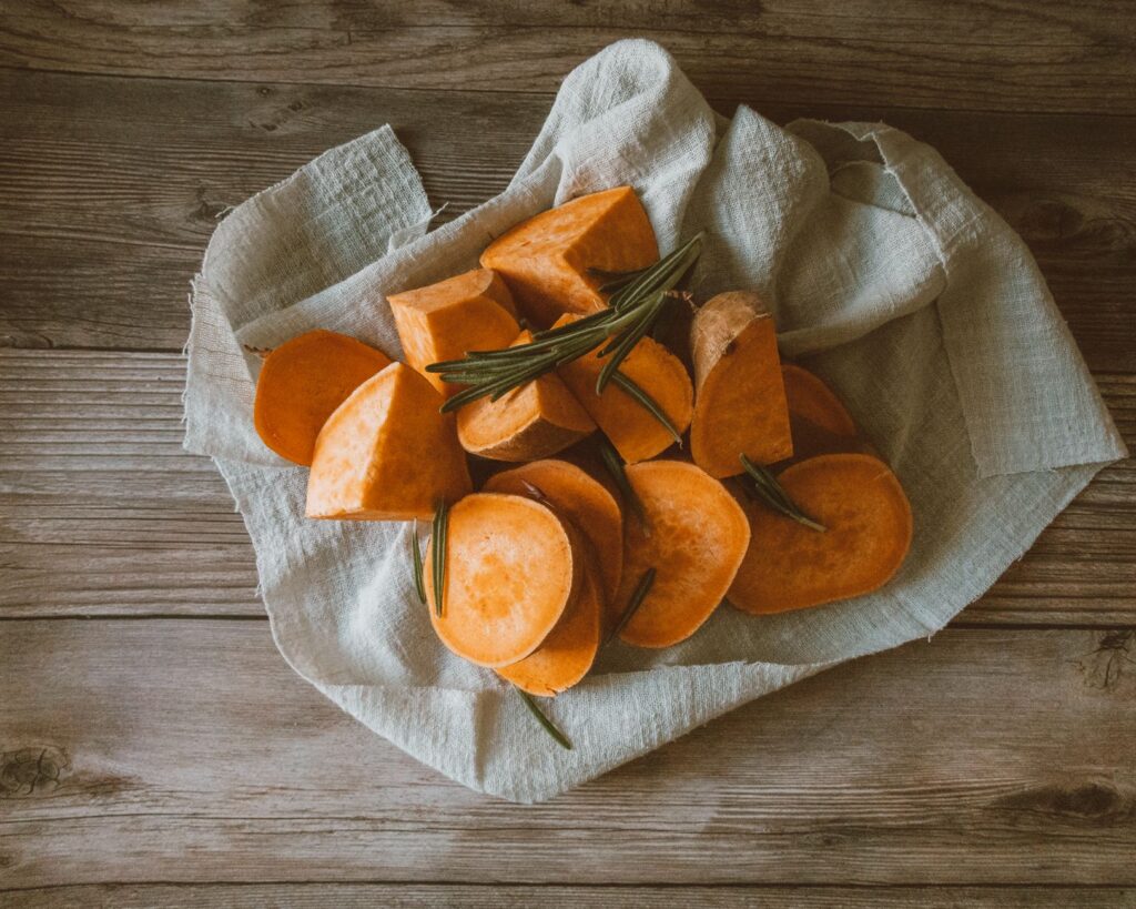 Un cadre rustique avec des patates douces tranchées sur une surface en bois, parfait pour des recettes d'automne.